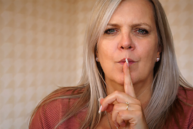 Eine Frau mit Finger vor dem Mund als Zeichen der Diskretion